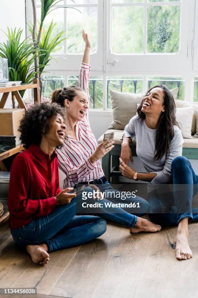 three carefree women sitting on the floor at home with cell phones - group on couch stock-fotos und bilder