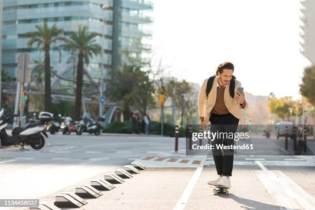 man looking at cell phone while skateboarding in the city - skateboard phone stock pictures, royalty-free photos & images