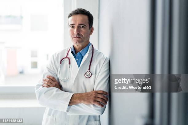 portrait of serious doctor leaning against a wall - arzt portrait stock-fotos und bilder
