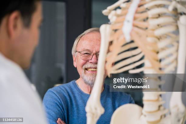 smiling senior patient with doctor in medical practice with anatomic model - anatomisches modell stock-fotos und bilder