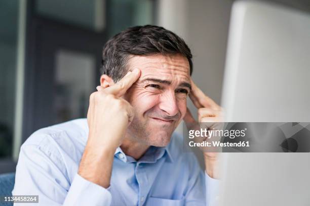 grimacing businessman looking at computer screen - man headache stock pictures, royalty-free photos & images