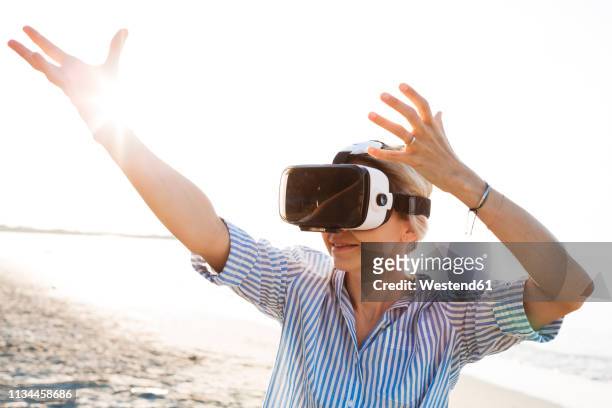 blonde woman doing kind of yoga exercises on a beach in thailand with 3d virtual reality goggles - new sport content fotografías e imágenes de stock