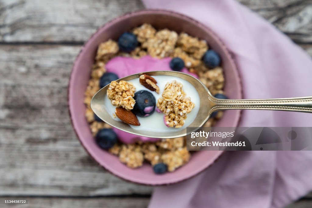 Granola, almonds, blueberry and milk on spoon, close-up