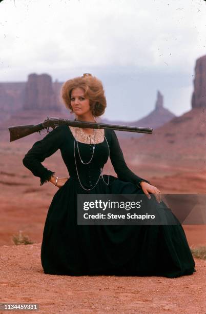 Portrait of Tunisian-born Italian actress Claudia Cardinale as she poses, a rifle balanced on her shoudler, in costume and on location in Monument...