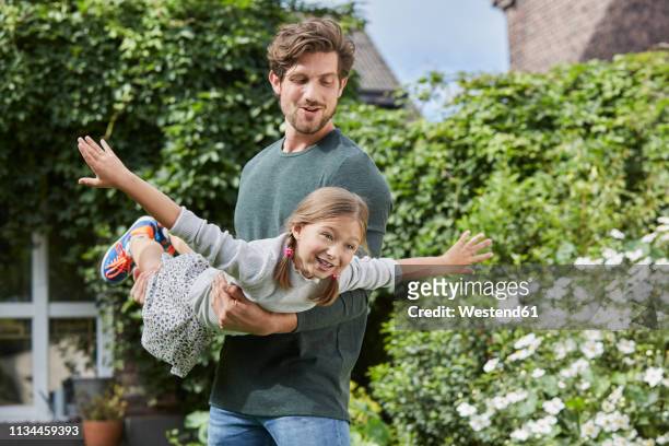 happy father playing with daughter in garden of their home - hacer el avión fotografías e imágenes de stock
