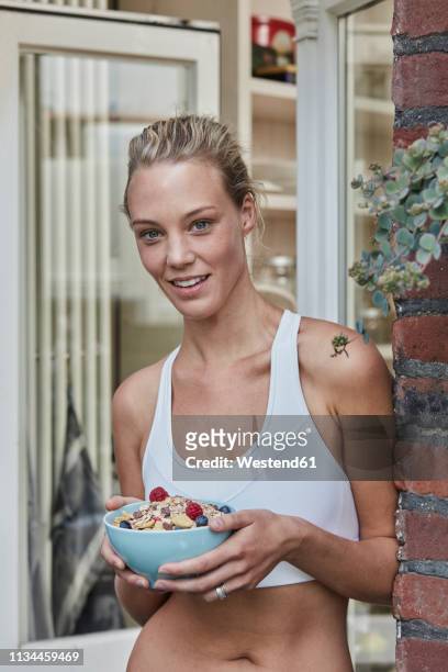 portrait of smiling sporty young woman with muesli bowl at house entrance - skinny blonde stock pictures, royalty-free photos & images