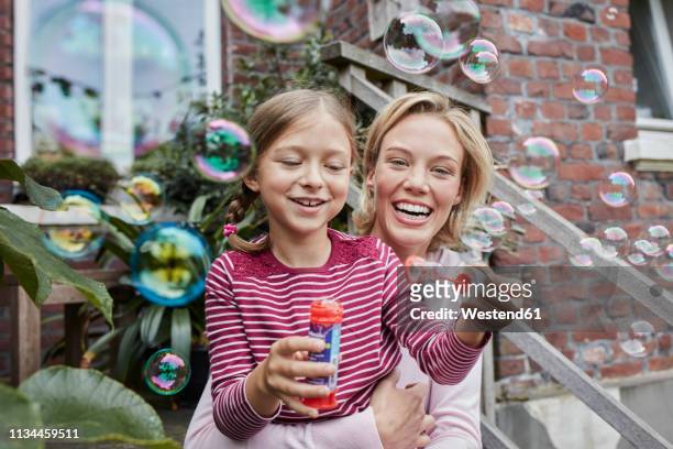 happy mother and daughter making soap bubbles - millennial generation stock-fotos und bilder