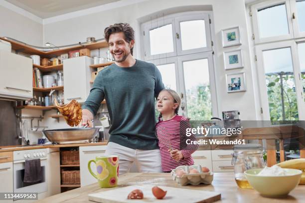 happy father and daughter baking pancakes in kitchen at home together - throwing foto e immagini stock