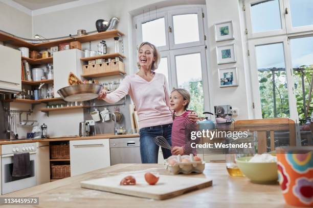 happy mother and daughter baking pancakes in kitchen at home together - pancake day foto e immagini stock