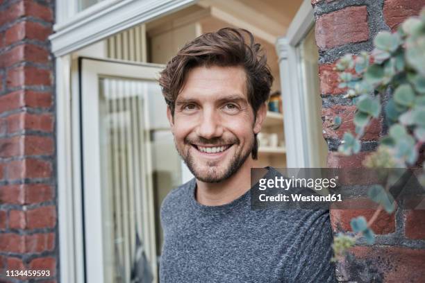 portrait of smiling man at house entrance - erwachsener über 30 stock-fotos und bilder