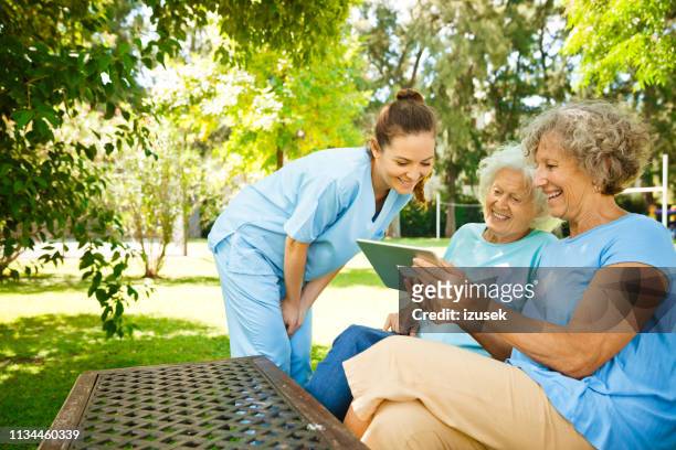 woman showing digital tablet to mother and nurse - assisted living community stock pictures, royalty-free photos & images