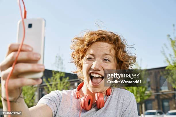playful young woman with headphones taking a selfie in urban surrounding - funny face stock pictures, royalty-free photos & images