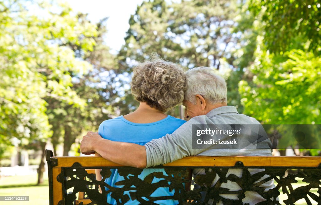 Retired man sitting with arm around woman on bench