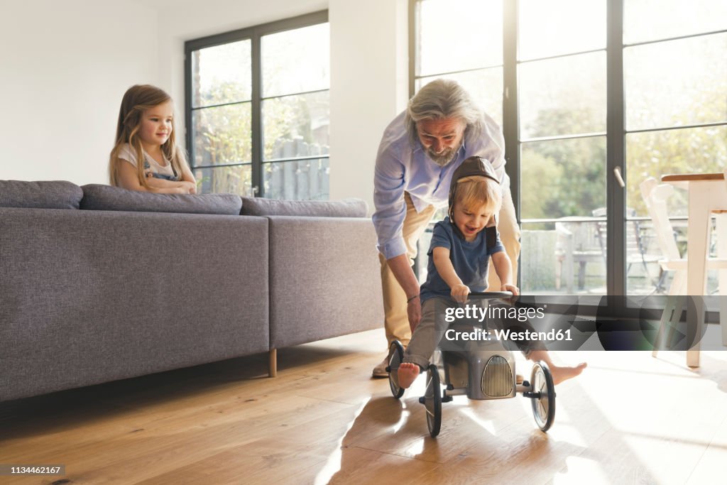 Grandfather playing with grandchildren, sitting on toy car