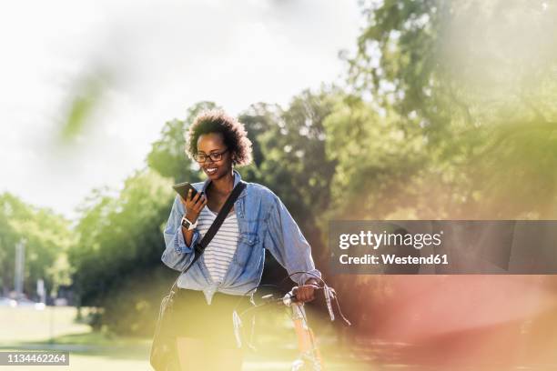 young woman with cell phone pushing bicycle in park - summer press day ストックフォトと画像