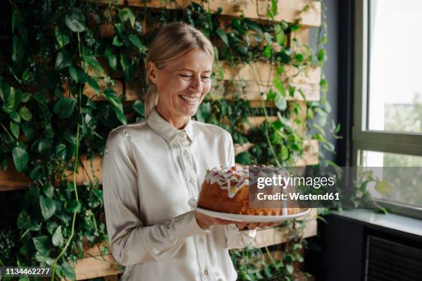 smiling businesswoman holding birthday cake in green office - happy birthday cake stock-fotos und bilder