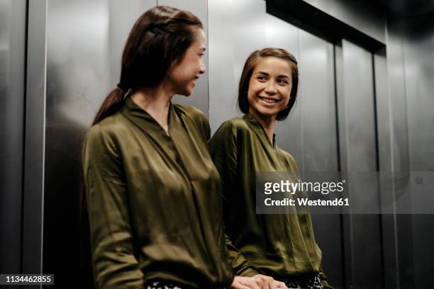 smiling young woman looking in mirror in elevator - mirror reflection stock pictures, royalty-free photos & images