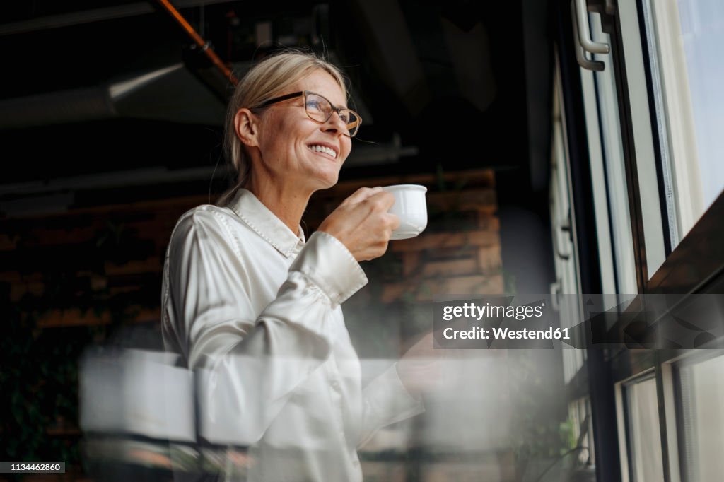 Smiling businesswomanholding cup of coffee looking out of window