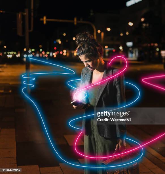 young woman looking at cell phone by night, composite - rosa germanica foto e immagini stock