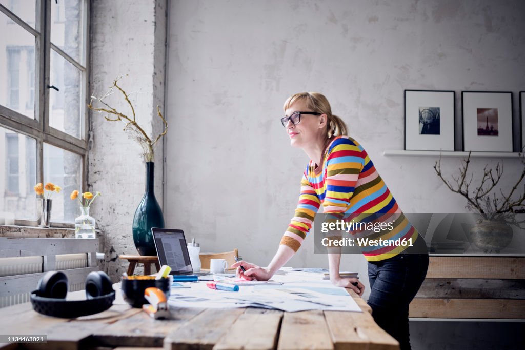 Portrait of smiling woman standing at desk in a loft looking through window