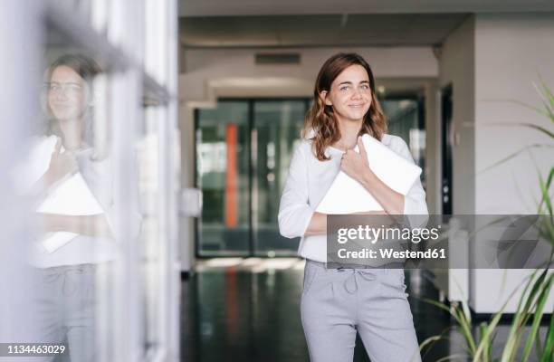 businesswoman standing in office, holding laptop - business education stock-fotos und bilder