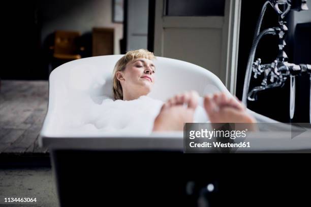 blond woman taking bubble bath in a loft - taking a bath stock pictures, royalty-free photos & images