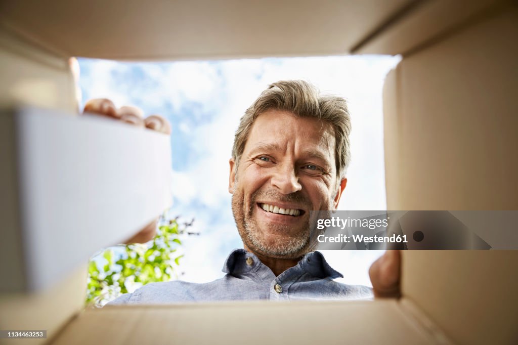 Mature man unpacking delivery, looking into box, smiling