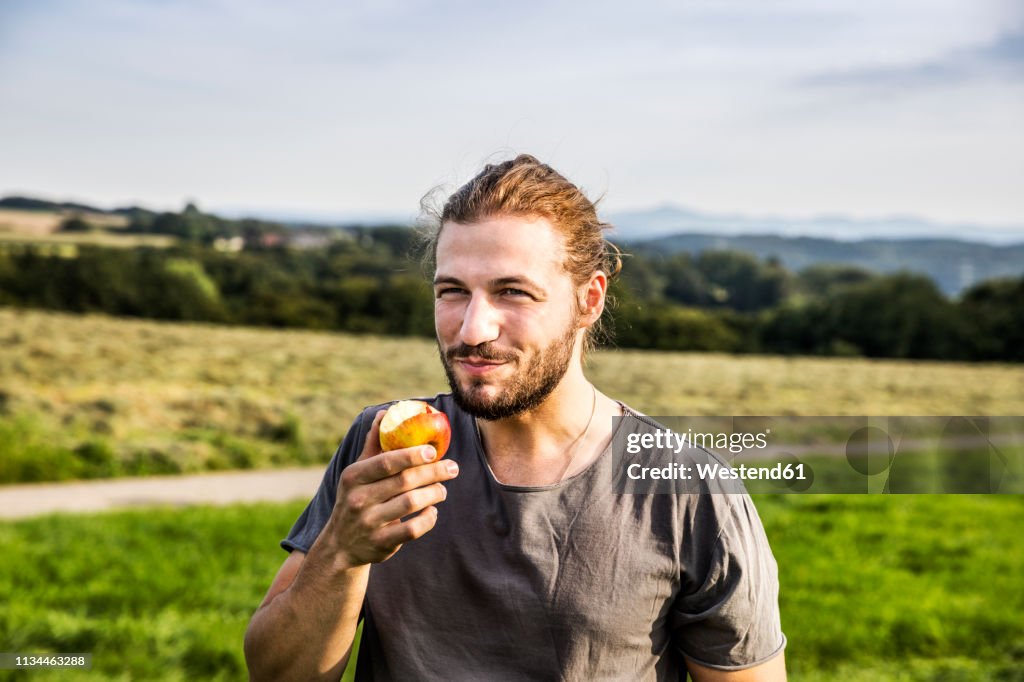 Young man eating an apple in rural landscape