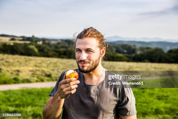 young man eating an apple in rural landscape - apple fruit 個照片及圖片檔