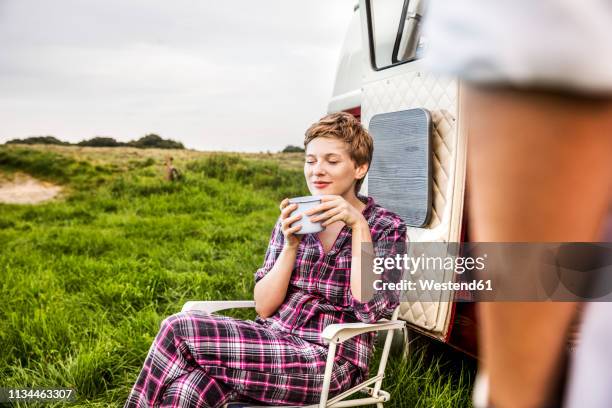 woman in pyjama enjoying coffee at a van in rural landscape - campingstuhl stock-fotos und bilder