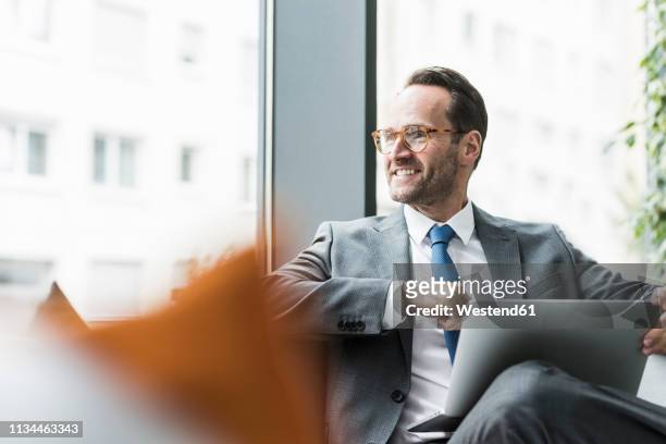 businessman sitting in lobby using laptop - finanzwirtschaft und industrie stock-fotos und bilder