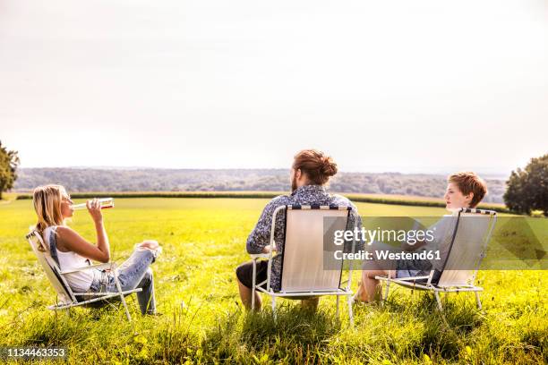 friends sitting on camping chairs in rural landscape - campingstuhl stock-fotos und bilder