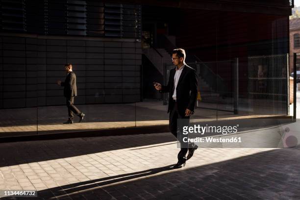 businessman walking in the city checking cell phone - business man walk stock-fotos und bilder