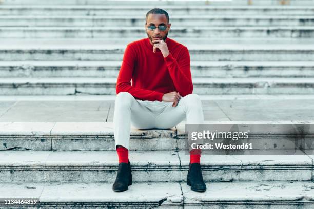 portrait of stylish young man wearing red pullover and socks sitting on stairs - menswear stock-fotos und bilder