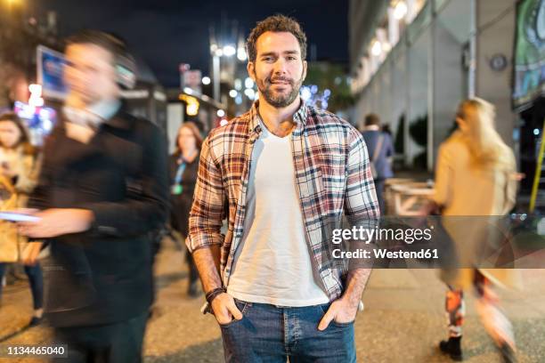 uk, london, portrait of a smiling commuter by night with blurred people passing nearby - people in crowd street imagens e fotografias de stock