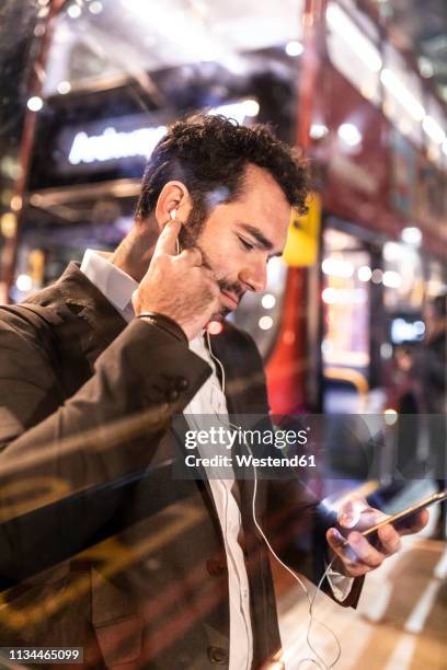 uk, london, businessman with cell phone and earbuds at the bus station by night - business forum in london stock-fotos und bilder