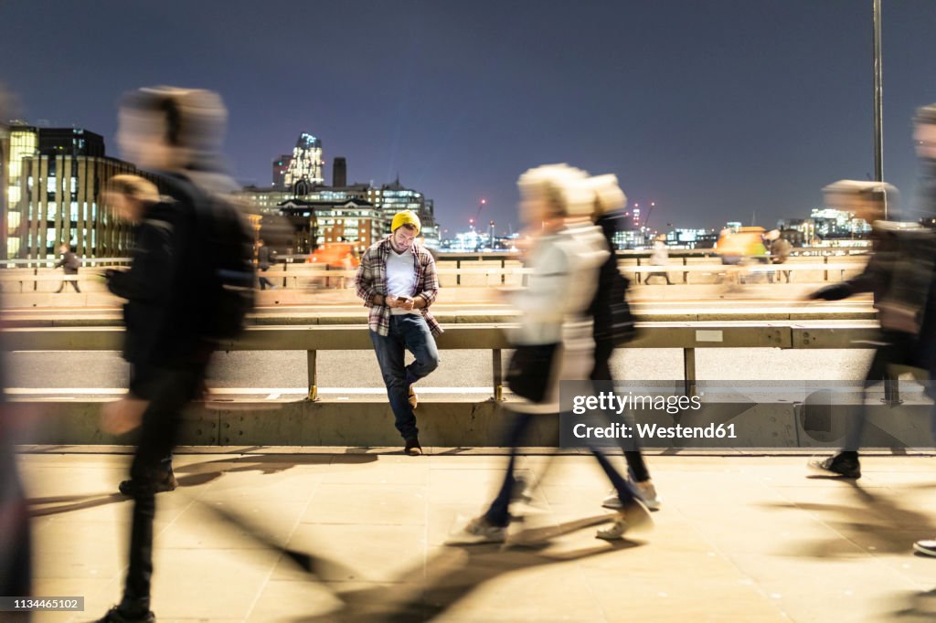 UK, London, man looking at his phone with blurred people walking on the pavement