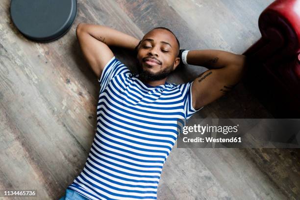 smiling young man lying on wooden floor with closed eyes - striped shirt stock pictures, royalty-free photos & images