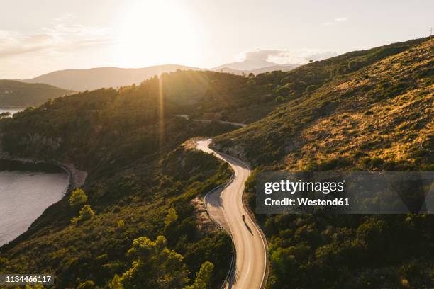 italy, elba island, biker on coastal road against the sun, aerial view with drone - adultes moto photos et images de collection