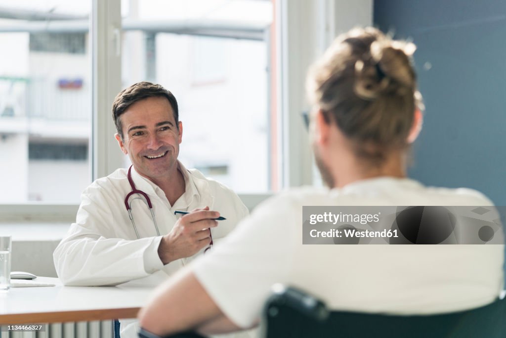 Smiling doctor talking to patient in wheelchair in medical practice