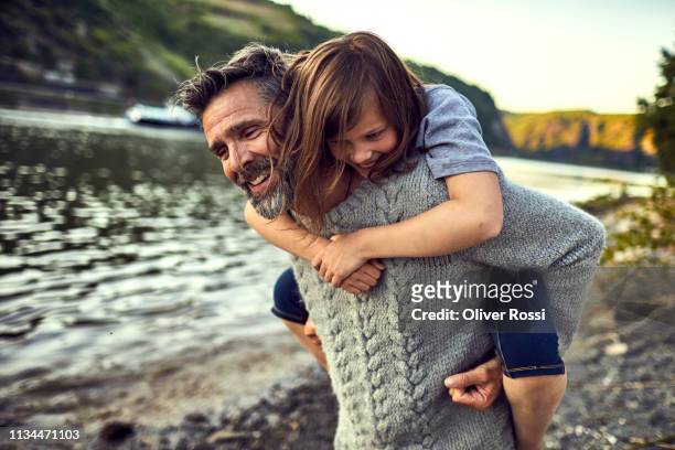 happy father carrying girl piggyback at the riverside - family caucasian fotografías e imágenes de stock