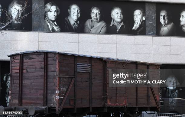 Portraits of Holocaust survivors are displayed on April 2, 2019 at the Museum of Jewish Heritage, as a vintage German train car, like those used to...