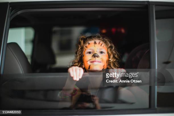 girl with tiger face looking out car window - face painting kids stock-fotos und bilder