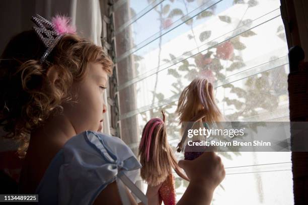female toddler looking out of window holding up dolls - dolls ストックフォトと画像