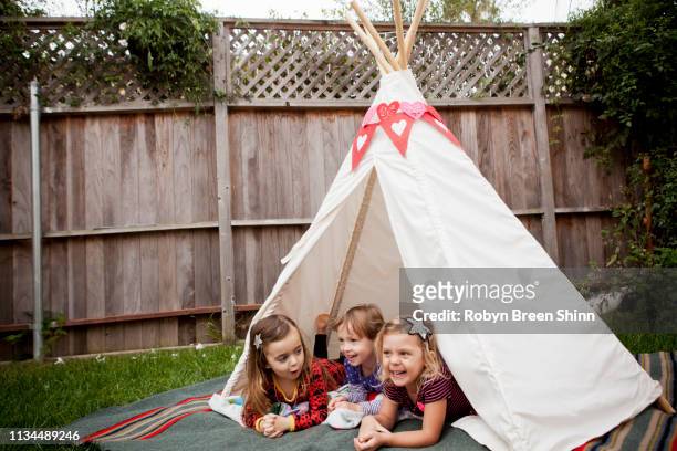 three young girls lying in teepee in garden - kampeertent stockfoto's en -beelden