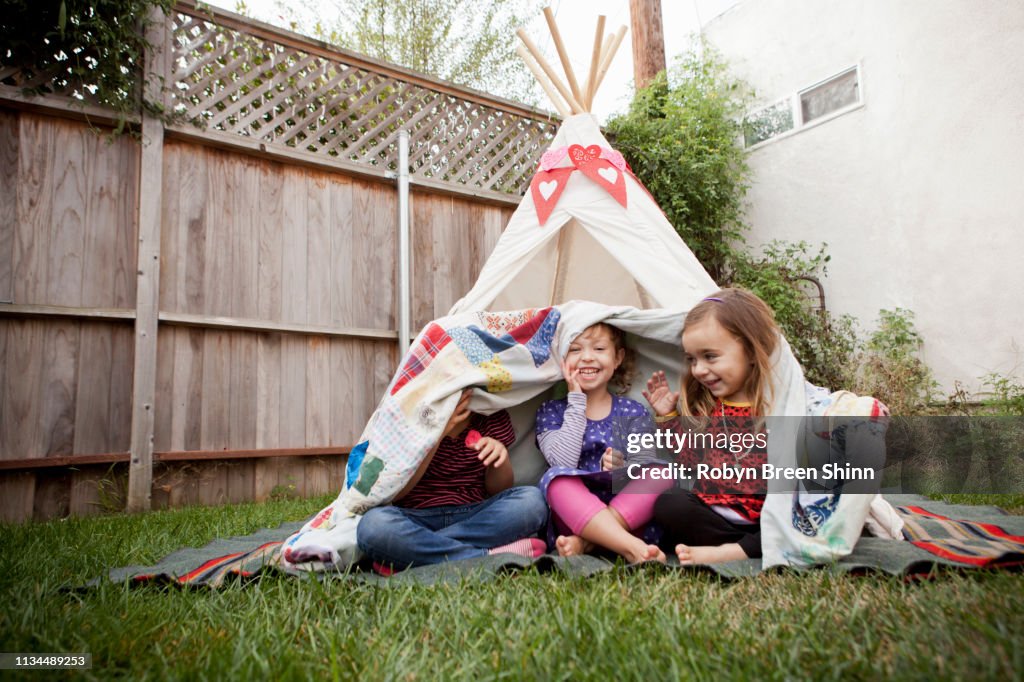 Three young girls in garden hiding under blanket
