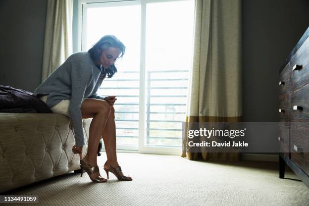 mature woman sitting on bed putting on high heels - high heel stockfoto's en -beelden