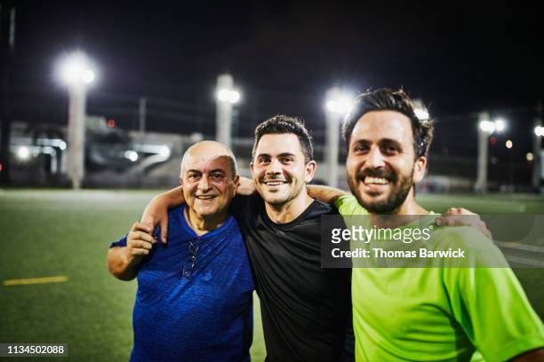 Smiling mature man embracing adult sons after evening soccer match