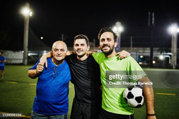 smiling mature man embracing adult sons after evening soccer match - family football team stock pictures, royalty-free photos & images