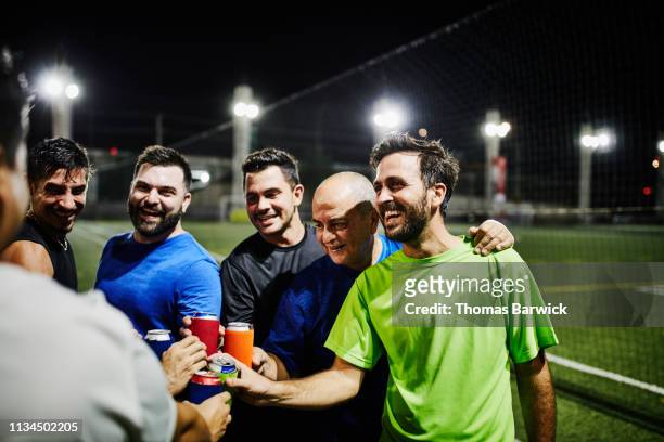 laughing male friends toasting with beers after nighttime soccer game - beer cheers stock-fotos und bilder